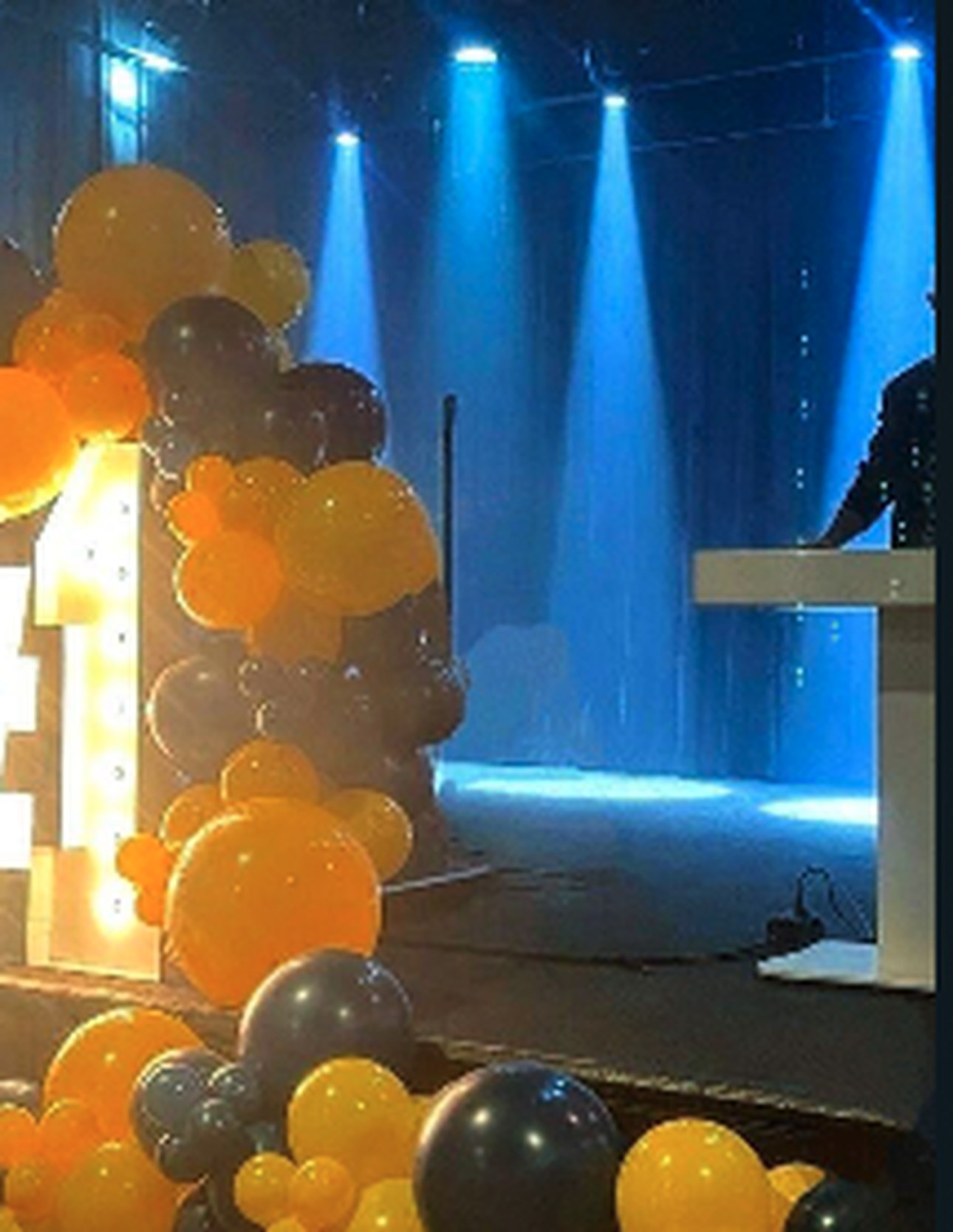 DJ on a pedestal booth beside a lit stage at a corporate holiday party
