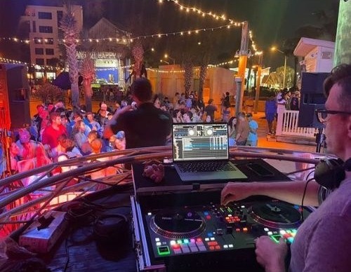 DJ Live playing to an outdoor crowd under string lights