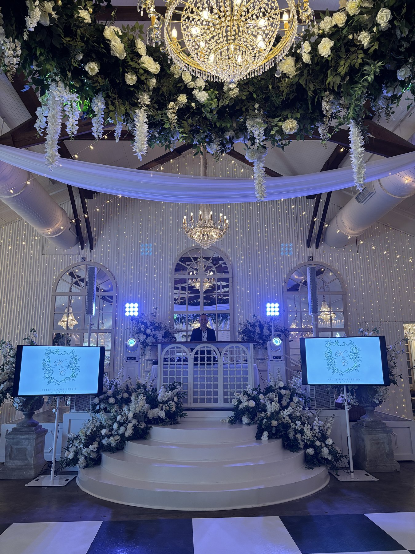 Screens, uplighting, and florals framing a ceremony stage