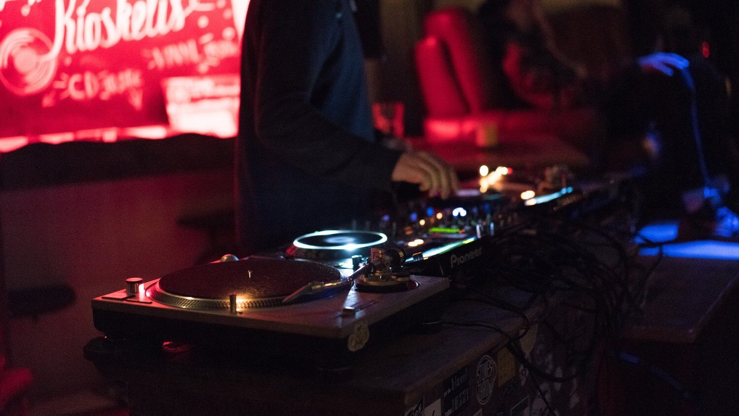 Turntables and a mixer lit red behind the booth