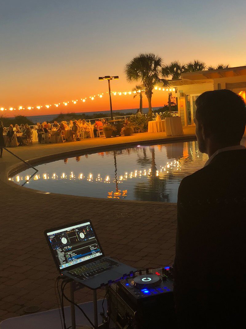 DJ booth overlooking a lit pool at sunset